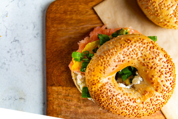 A sandwich made of sesame bagel, smoked salmon, white cheese on a cutting board. A breakfast composition, top view.