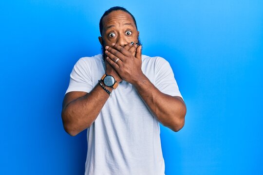 Young african american man wearing casual white tshirt shocked covering mouth with hands for mistake. secret concept.