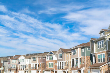 Three storey townhouses with garages at the facade against clouds and blue sky