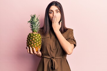 Young beautiful girl holding pineapple covering mouth with hand, shocked and afraid for mistake....