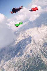 Tandem wingsuit fliers glide over mountains at sunrise