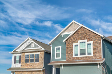 Gabled homes with stone brick and wooden siding on walls against cloudy blue sky