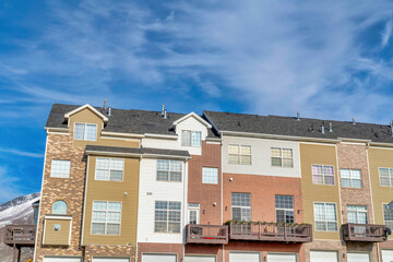 Townhomes with balconies and wide garage doors against blue sky with clouds