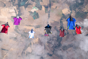 Team of wingsuit fliers glide in formation at sunset