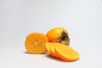 One whole from back and one half persimmon fruits with slices next to each other on white background - portrait