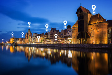 Map pin icons on Long Bridge waterfront in Gdansk at dusk. Lit Crane and other old buildings along...