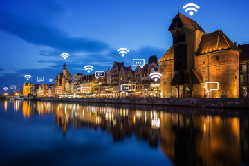 Obraz premium Lit Crane and other old buildings along the Long Bridge waterfront at the Main Town in Gdansk, Poland, at dusk. Wireless network connection, WiFi, smart city and online messaging concept.