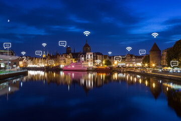 Motlawa River and lit old buildings on the Long Bridge waterfront at the Main Town (Old Town) in Gdansk, Poland, at dusk. Wireless network connection, WiFi, smart city and online messaging concept. 