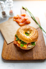 A breakfast composition. A sandwich made of sesame bagel, smoked salmon, white cheese on a cutting board. 