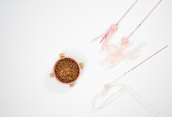 dry cat food in a ceramic pink bowl on a bamboo stand and pink toys teasers on a white background