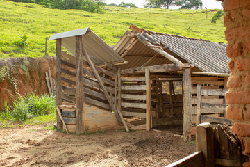 A kind of barn on a corral, after a heavy rain with the ground full of puddles. In the background there are a green pasture and blue sky