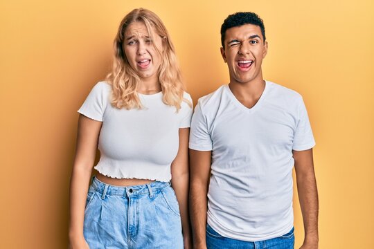 Young interracial couple wearing casual white tshirt winking looking at the camera with sexy expression, cheerful and happy face.