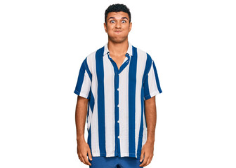 Young arab man wearing casual clothes puffing cheeks with funny face. mouth inflated with air,...