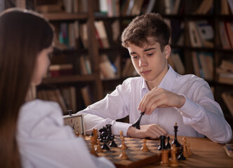 A boy and a girl play chess, teenagers play a board game, sports interest, schoolchildren are sitting at the table, learning to play chess.  © malyutinaanna