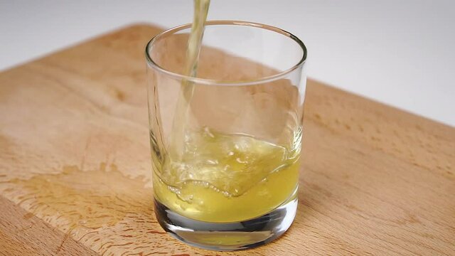 Low alcohol cider is poured into a glass on a wooden board in slow motion.