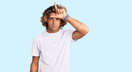 Young hispanic man wearing casual white tshirt making fun of people with fingers on forehead doing...