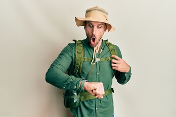 Fototapeta premium Handsome man with beard wearing explorer hat and backpack looking at the watch time worried, afraid of getting late