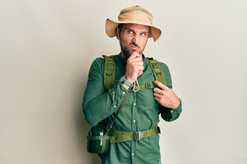 Handsome man with beard wearing explorer hat and backpack thinking worried about a question,...