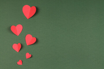 Red paper hearts on a green background. Valentine's Day.