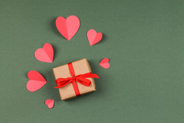 Gift box with bow and paper hearts on a green background. Valentine's Day.