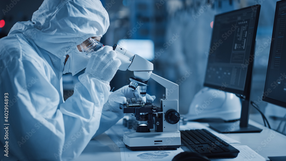 Poster research factory cleanroom: engineer / scientist wearing coverall, gloves uses microscope to inspect