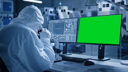 Research Factory Cleanroom: Close-up of Engineer / Scientist wearing Coverall and Gloves Uses Microscope, Computer Has Chroma Key Green Screen Display. Scientific and Electronics Research Facility