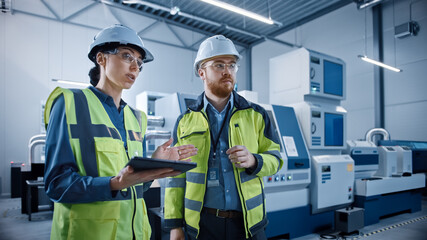 Modern Factory: Female Project Manager and Male Engineer Standing Wearing Safety Jackets, Hard...