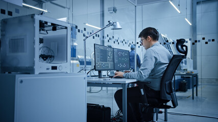 Factory Office: Portrait of Beautiful and Confident Male Industrial Engineer Working on Computer, on Screen Industrial Electronics Design Software. High Tech Facility with CNC Machinery