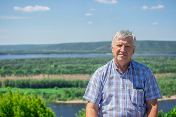 Naklejka na ściany i meble Portrait of a handsome senior man with a beautiful river landscape on the background. Happy old man relaxing outdoor. 