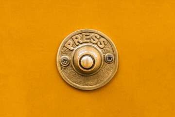 Vintage style solid golden brass metal doorbell button against a seamless bright yellow painted...