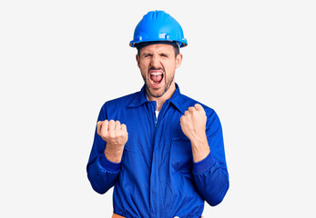 Young handsome man wearing worker uniform and hardhat celebrating surprised and amazed for success with arms raised and eyes closed. winner concept.
