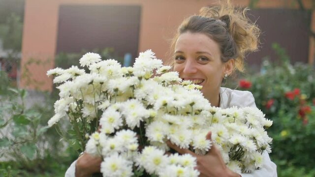 Pretty young girl is standing near a bush of white chrysanthemums in park during spring time, hypersensitivity, asthma, or allergy concept
