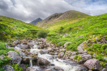 Winding mountain stream or river in Cronins Yard. Green valley with Carrauntoohil in a distance, the highest mountain in Ireland, Ring of Kerry