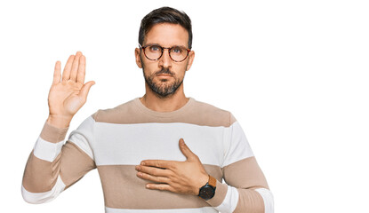 Handsome man with beard wearing casual clothes and glasses swearing with hand on chest and open...