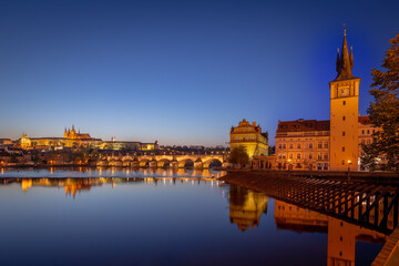 Fototapeta na wymiar View on Charles Bridge and Prague Castle over Vltava River during early night with wonderful blue sky and yellow city lights, Czechia, Europe