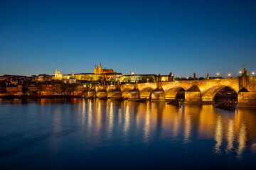 View on Charles Bridge and Prague Castle over Vltava River during early night with wonderful blue sky and yellow city lights, Czechia, Europe