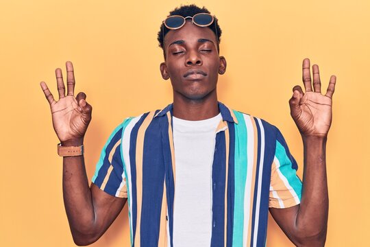 Young african american man wearing summer clothes and sunglasses relax and smiling with eyes closed doing meditation gesture with fingers. yoga concept.