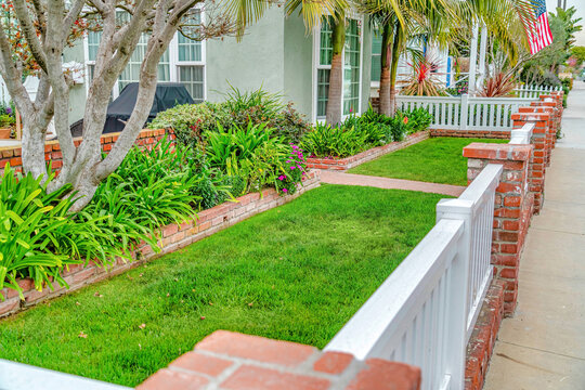 Front yard of home with green lawn pathway wooden fence and red brick posts