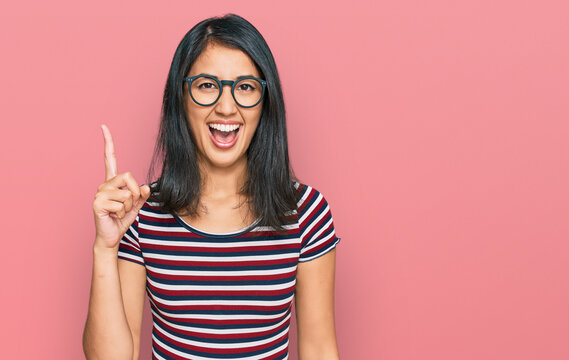 Beautiful asian young woman wearing casual clothes and glasses pointing finger up with successful idea. exited and happy. number one.