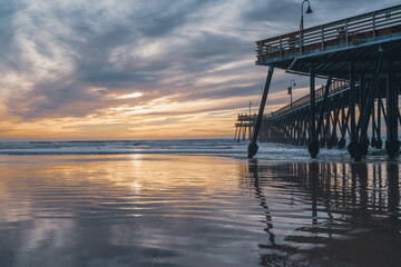 Pismo Beach, California/USA - January 1, 2021  Pismo Beach sunset. Wooden pier, a famous touristic attraction, wide sandy beach, Pacific ocean, and beautiful cloudy sky
