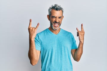 Naklejka premium Middle age grey-haired man wearing casual clothes shouting with crazy expression doing rock symbol with hands up. music star. heavy concept.