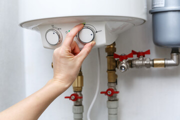 Female hand puts thermostat of electric water heater (boiler) in a high power consumption mode.