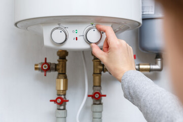 Female hand puts thermostat of electric water heater (boiler) in economy mode. - 402919889