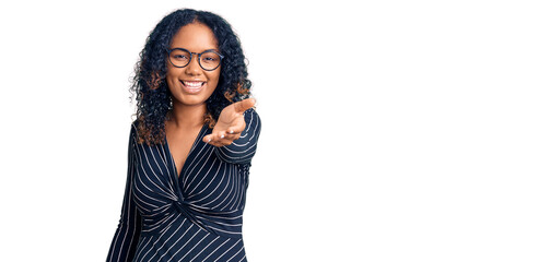 Young african american woman wearing casual clothes and glasses smiling friendly offering handshake as greeting and welcoming. successful business.