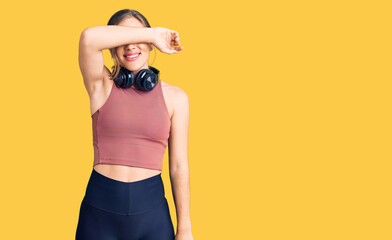 Beautiful caucasian young woman wearing gym clothes and using headphones covering eyes with arm smiling cheerful and funny. blind concept.