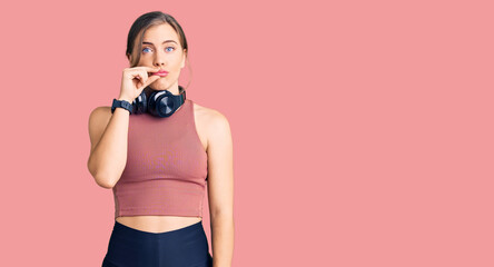 Beautiful caucasian young woman wearing gym clothes and using headphones mouth and lips shut as zip...