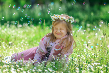 Summer portrait of happy cute child in flower meadow. Girl with wreath of daisies on her head in...