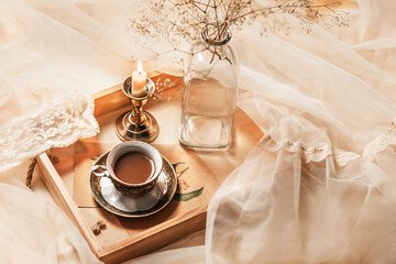 Coffee in bed, romantic atmosphere. Flowers in a vase, a burning candle and a cup of coffee on a wooden tray on a silk bed. Home interior, lifestyle. Selective focus