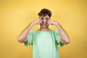 Fototapeta na wymiar Handsome man wearing a green casual t-shirt over yellow background depressed and worry for distress, crying angry and afraid. Sad expression.