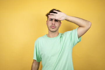 Fototapeta na wymiar Handsome man wearing a green casual t-shirt over yellow background Touching forehead for illness and fever, flu and cold, virus sick